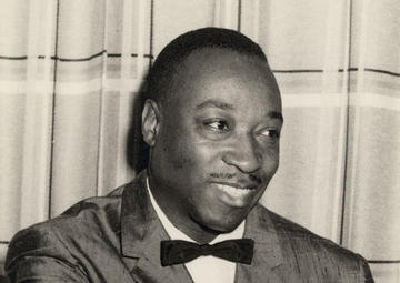 Musician Dave Bartholomew smiles and looks to his left while sitting in a chair in a tux