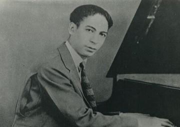 Jelly Roll looks at the camera while he plays the piano in a black-and-white picture