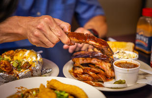 A table filled with Louisiana barbecue, including ribs, sliced sausage, beans, coleslaw and a stuffed baked potato at Cou-Yon's Cajun Bar-B-Q.