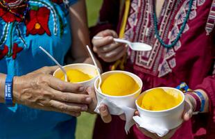 Hands hold three bright orange mango freezes at the New Orleans Jazz & Heritage Festival.