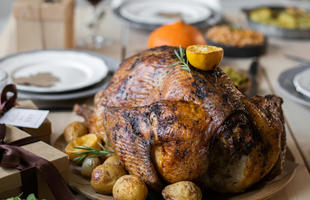 A perfectly roasted Louisiana turducken, topped with a sprig of thyme and half a lemon, surrounded by roasted potatoes, on a neatly set Thanksgiving table.