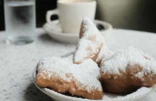 a vegan beignet on a plate with a coffee cup behind it