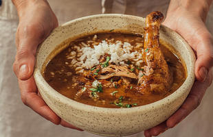 A pair of hands present a bowl filled with rice and chicken in a red sauce from the Mosquito Supper Club in New Orleans.