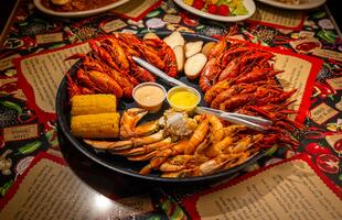 A large platter of seafood, including crawfish, corn and potatoes on a brightly decorated table at Boudreau &amp; Thibodeau’s Cajun Cookin’.