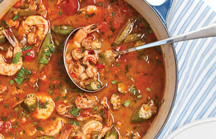 On a table in Louisiana, a silver ladle sits in a blue crockpot ready to scoop out red broth ladened with shrimp, crawfish, okra and spices.